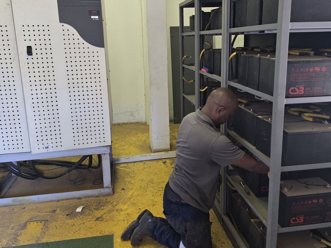 Technician replacing cells in a UPS battery bank beside an APC UPS